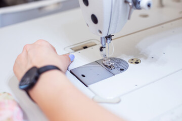 a female seamstress inserts a thread into a needle on a sewing machine. The dressmaker works on a sewing machine. A tailor sews clothes at his workplace. Hobby sewing as a small business concept