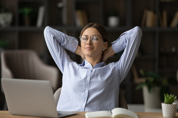 Calm millennial woman sit at desk at office relax finish computer work on time. Happy young Caucasian female employee rest at workplace relieve negative emotions daydream. Business vision concept.