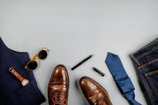 Men Clothes Concept. Vintage Style. Flat Lay on Light Grey Background. Included Wingtips Dress Shoes, Hand Watch, Pen, Necktie, Jeans and Sunglasses . Stylish Men. Top View