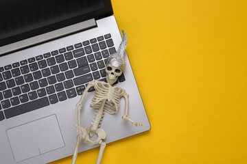Skeleton in foil hat and laptop on yellow background. Conspiracy - obrazy, fototapety, plakaty