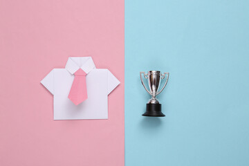 Origami shirt with tie and winner cup.on blue pink background. Leadership, business concept