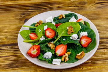 Fresh healthy salad with strawberry, spinach, walnuts and feta cheese on wooden table