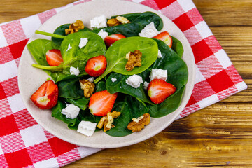 Fresh healthy salad with strawberry, spinach, walnuts and feta cheese on wooden table