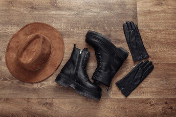 Women's accessories. Black Leather boots, gloves and hat on wooden floor. Top view. Flat lay