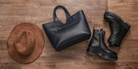 Women's accessories. Black Leather boots, bag and hat on wooden floor. Top view. Flat lay