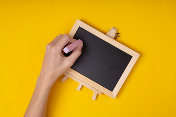 Woman draws writes with chalk on a mini chalk board on a yellow background. School, education concept
