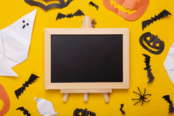 Mini blank chalk board with copy space and halloween decor on yellow background. Trick or treat. Flat lay