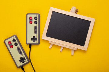 Retro gamepad and Blank mini chalkboard with copy space on a yellow background. Gaming concept. Top view. Flat lay