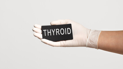 Closeup of the hand in a white sterile glove holding a card with word - THYROID
