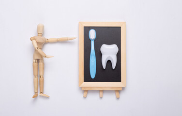 A puppet points to a chalk board with a tooth, a toothbrush on a white background. Dental care concept