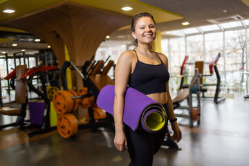 Fototapeta premium Young attractive fit woman with mat in her hands in gym
