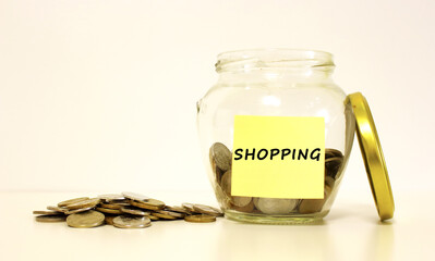 Glass jar with coins for savings. The inscription SHOPPING on the note paper.