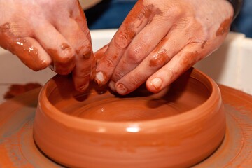 The master potter uses his fingertips to shape the edges of the earthenware bowl on the potter's wheel in the workshop