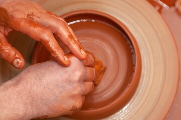 Fototapeta premium A bowl of orange clay rotates on a potter's wheel. In the hands of a master potter, a sponge is used to grind a pottery