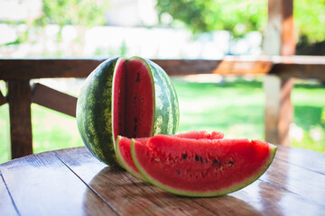 Sliced watermelon on a wooden table in the garden on a background of trees in the gazebo