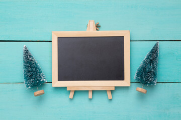 Toy Christmas trees and Blank mini chalk board on a light blue wooden background. Copy space