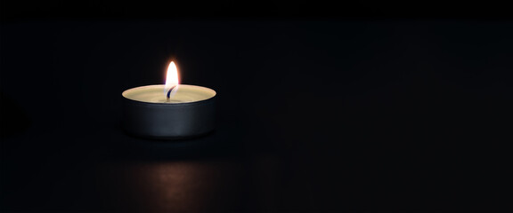 A burning candle on a dark background with a flare in the foreground.