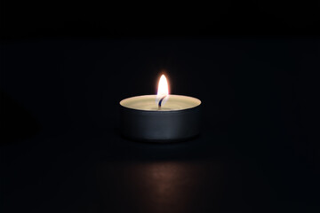 A burning candle on a dark background with a flare in the foreground.
