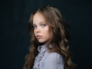 Fototapeta premium portrait of a beautiful girl in a gray dress on a dark background and curly hair blue eyes