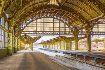 Naklejka na ściany i meble View of the old railway station with a large metal arch and an empty platform with a clock.