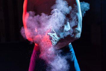 Weightlifter claps hands with talcum powder and prepares for workout in red blue gradient neon...
