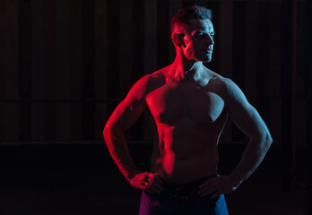 Fototapeta na wymiar Athletic handsome man athlete with naked torso in red blue gradient neon light on black background