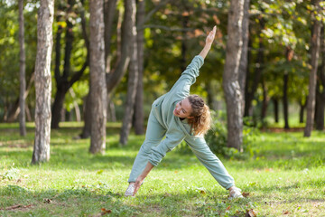 Attractive fit slim Caucasian woman with curly hair in sportswear doing warm up exercise in the park or forest  at bright sunny day. Healthy lifestyle