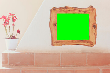 A picture frame made of olive wood, hanging from a fireplace in a country-style house, with a green frame in it (replace with your own content).
