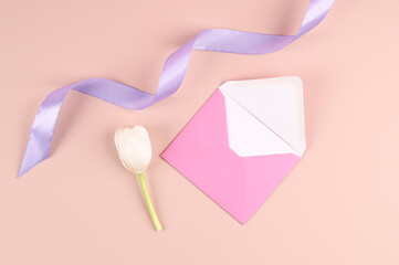 Womens day, birthday, wedding day and other festive background, card. Pink envelope, tulip and silk ribbon on pastel pink table.