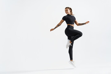 Woman in sportwear doing jump workout and look behind at empty space for logo. Female athlete with fit body exercising on white background, training with happy smile