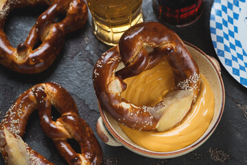 Beige bowl with cheese dip, pretzels and beer, studio shot on a brown stone background
