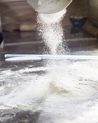 Obraz premium White flour is poured onto a metal table through a sieve. Sifting flour for dough