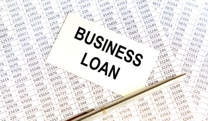 Obraz premium On the business card the text of Business Loan, next to the pen, the background are reports.