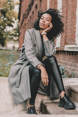 Portrait of an African American woman who sits on the steps near the building and poses