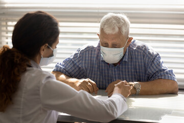 Obraz premium Close up female therapist consulting mature man patient wearing medical face mask about health insurance agreement, contract terms, discussing checkup results, prescriptions, healthcare concept
