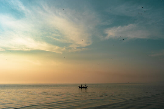 Traditional fishing boat floating alone in the sea with seagulls flying above before sunrise in the morning