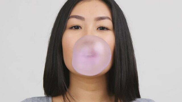 Asian Young Woman Chewing And Blowing Bubble-Gum, White Background