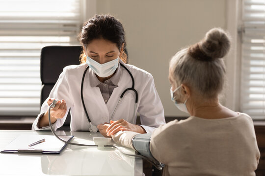 Close Up Serious Female Doctor Wearing Face Mask Measuring Checking Old Woman Blood Pressure, Using Digital Tonometer, Medical Checkup, Elderly Generation Healthcare And Insurance Concept