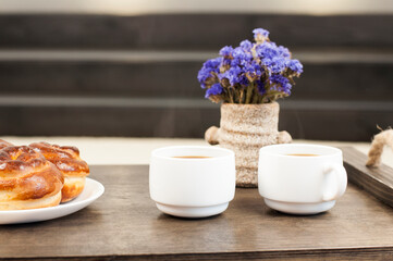 Two cups of coffee on a tray. A bun and a bouquet of flowers. Breakfast in bed.