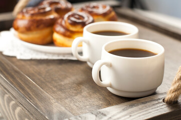 Two cups of coffee on a tray. A bun and a bouquet of flowers. Breakfast in bed.