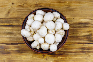 Fototapeta na wymiar Fresh champignon mushrooms in ceramic bowl on the wooden table. Top view