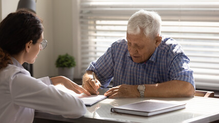Close up mature man signing contract in doctor office, female therapist physician pointing finger at document, senior patient making health insurance deal, putting signature, healthcare concept