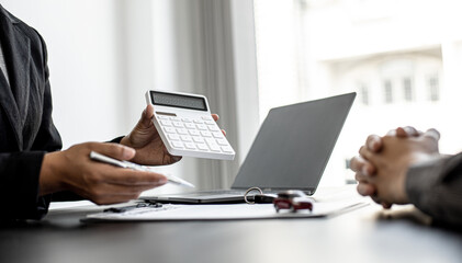 A car rental company employee holds a white calculator to show the tenant the rental price, the employee calculates the cost of the car rental before entering into the lease agreement with the renter.