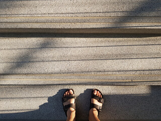 Close up feet of man in brown fashion sandals for outdoor stand on steps in sunny day.