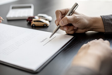 A close-up picture of the tenant who is about to sign the signature on the car rental contract with the car rental company after discussing the details with the employee. Concept of car rental.