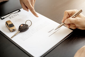 An employee of the rental car company points to the contract document in the Renter's signature box to have the tenant sign the rental agreement to agree to the rental agreement. Concept car rental.