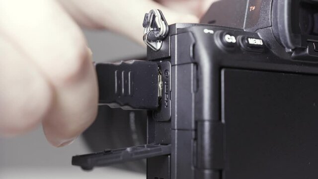 Close up of male hand inserting HDMI cable into a professional camera and taking it out isolated on grey background. Action. Details of shooting equipment.