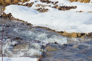 Winter river. Water flow and snowy shores. Thaw. Early spring