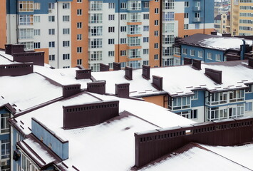 The roof with a chimney is covered with snow in winter. Tall houses in a big city in winter