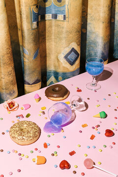 Minimal after party concept with small ice cream, pink creative drink in wine glasses, candies and lolly pop all over the pink table background and gold silk or saten curtain.